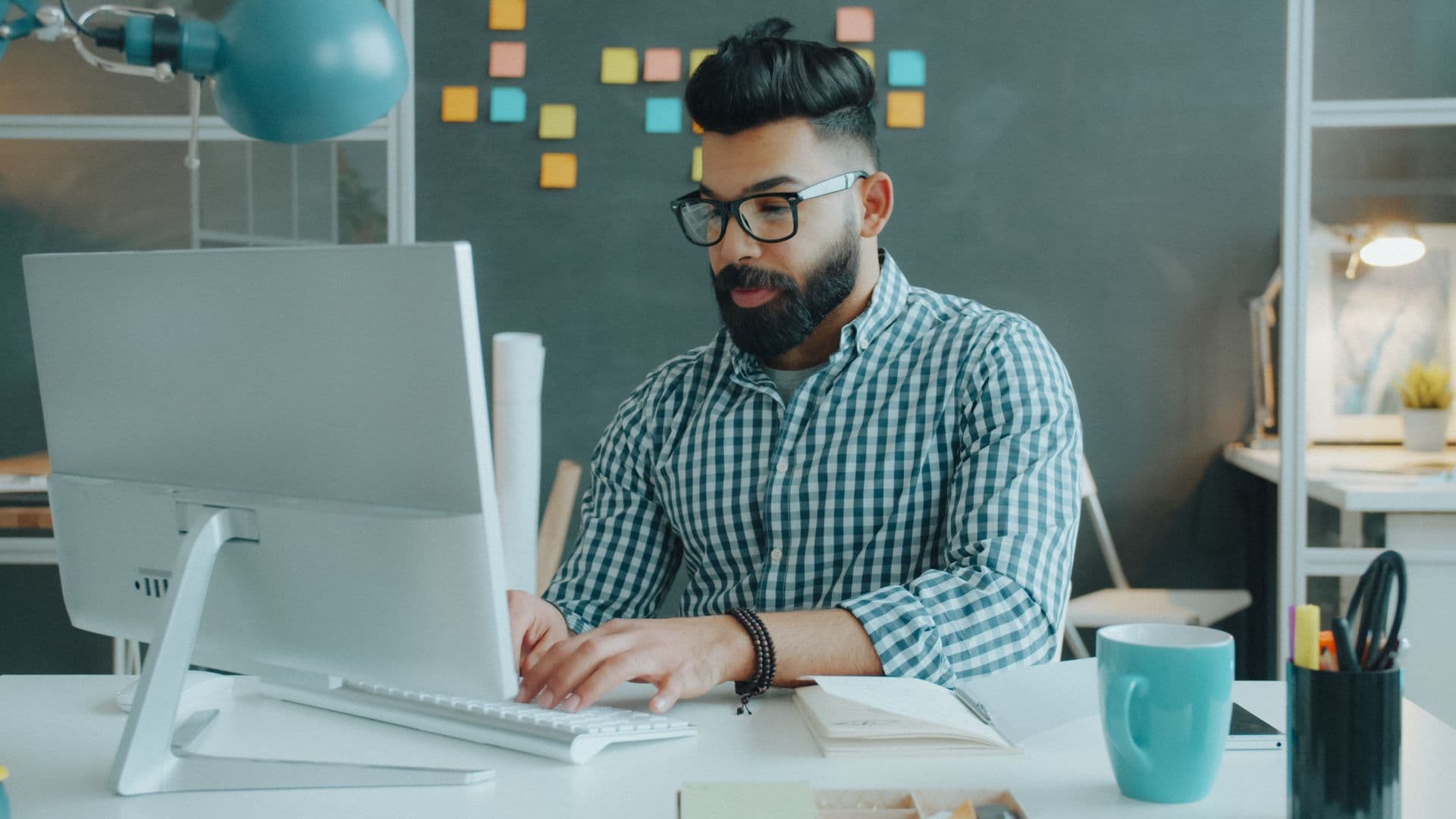 Man with glasses and a beard typing at a desktop computer