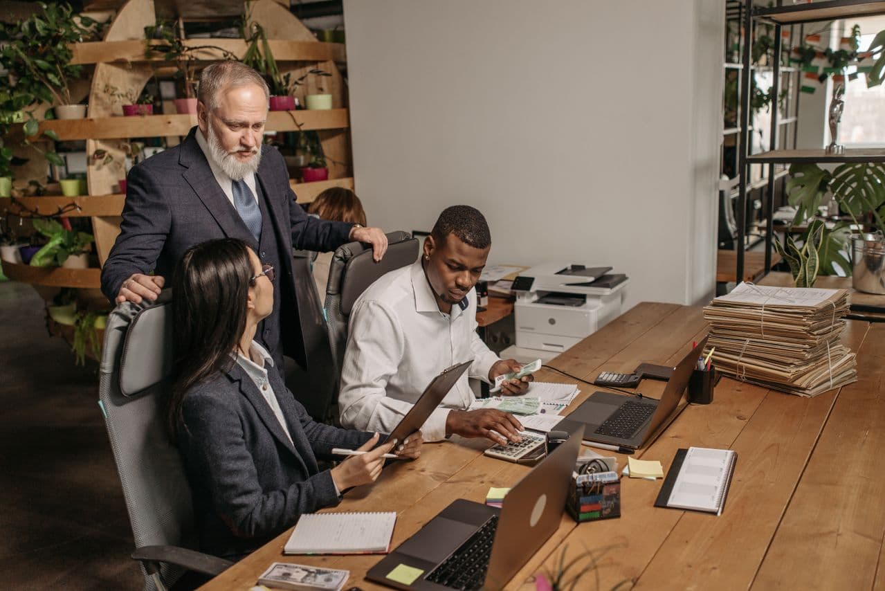 Manager standing over two colleagues reviewing documents at a desk